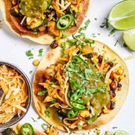 Black bean tostadas topped with corn, salsa, and veggies served on a white cutting board.