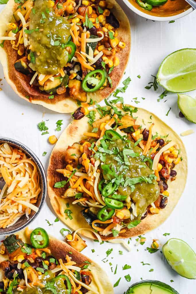 healthy vegetarian black bean tostadas served on a white cutting board, topped with cheese and tomatillo salsa