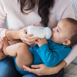 probiotics for baby constipation - Little infant baby lying on mothers hand drinking milk from bottle. Newborn baby drinking milk from bottle. Cute toddler with milk bottle on leg of mother.