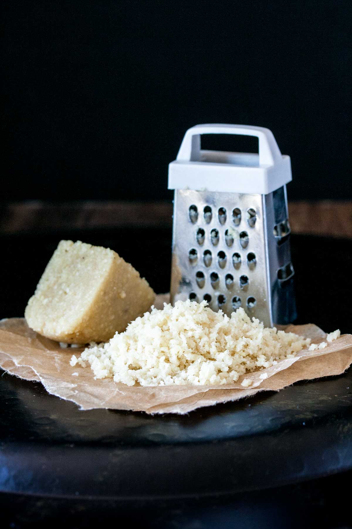 A pile of grated Parmesan next to a grater and a piece of the cheese block