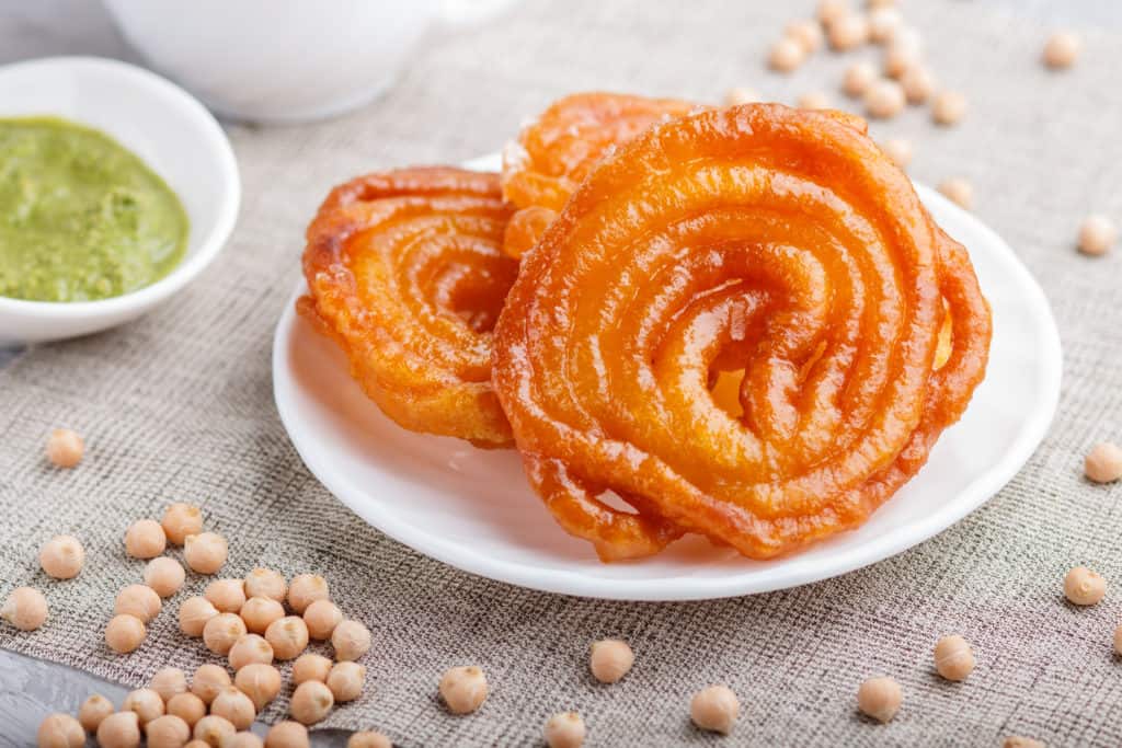 traditional indian candy jalebi/Imarti in white plate with mint chutney on a gray concrete background. side view, close up.