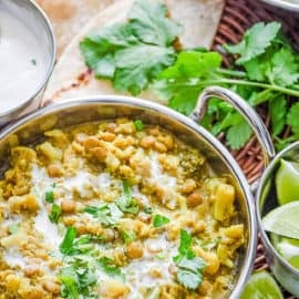 Lentil Cauilflower Curry served in a stainless steel pot with naan, cilantro and rice on the side