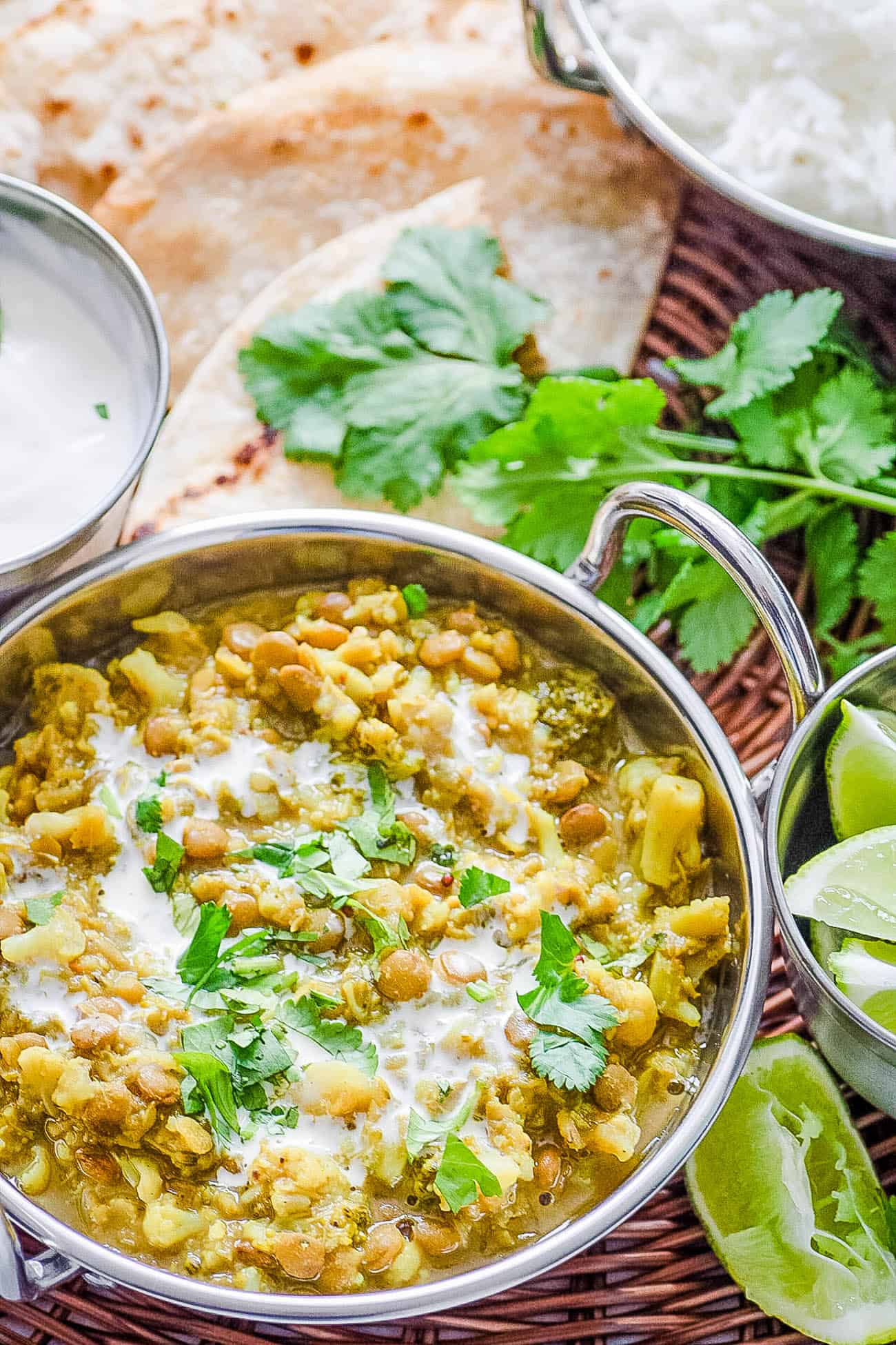 Lentil Cauilflower Curry served in a stainless steel pot with naan, cilantro and rice on the side