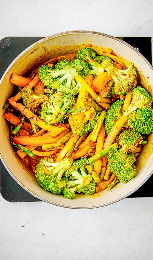 Veggies cooking in a ، with curry seasonings.