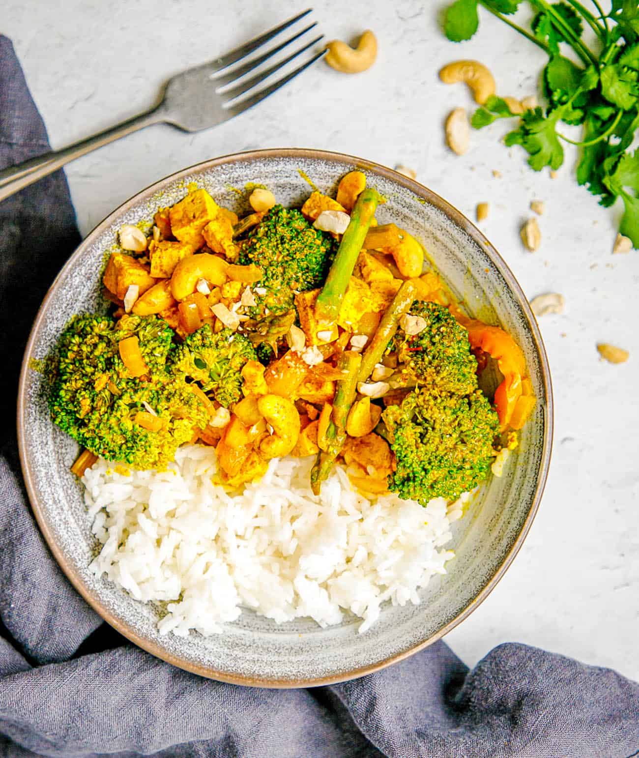 Tofu Yellow Curry with Veggies and Cashews served in a grey bowl with white rice