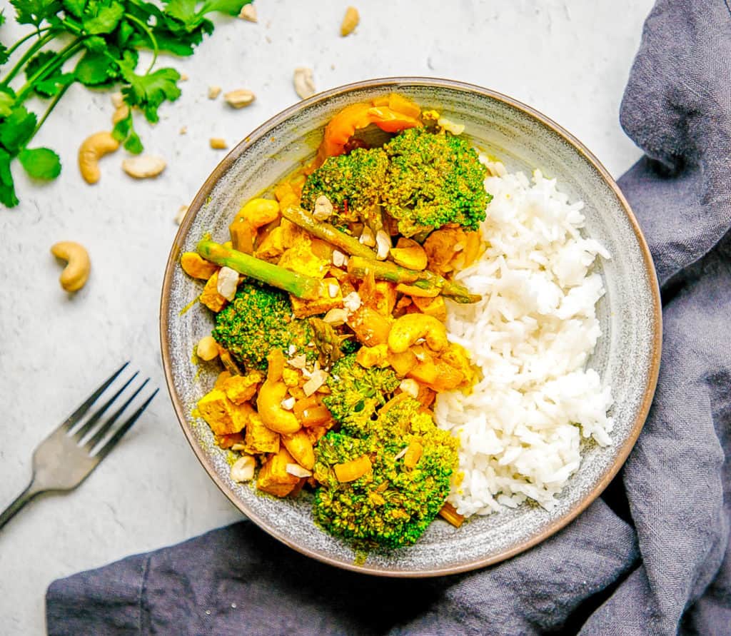 Tofu Yellow Curry with Veggies and Cashews served in a grey bowl with white rice