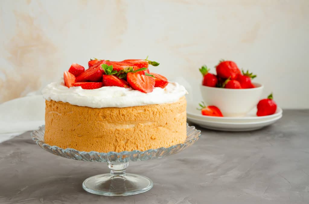 Angel food cake with whipped cream and slices of fresh strawberries on top on a concrete background. Summer dessert. Horizontal orientation, copy space - foods that start with a