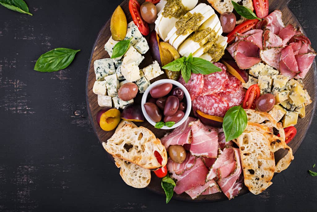 Antipasto platter with ham, prosciutto, salami, blue cheese, mozzarella with pesto and olives on a wooden background. Top view, overhead
