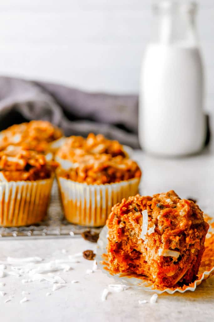 Apple carrot cinnamon muffins on the counter with a bite taken out of one of them.