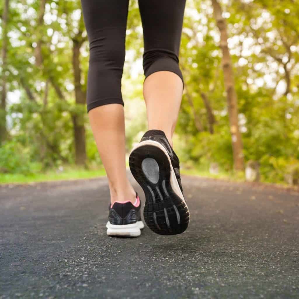 woman's legs and feet running on black top in the woods