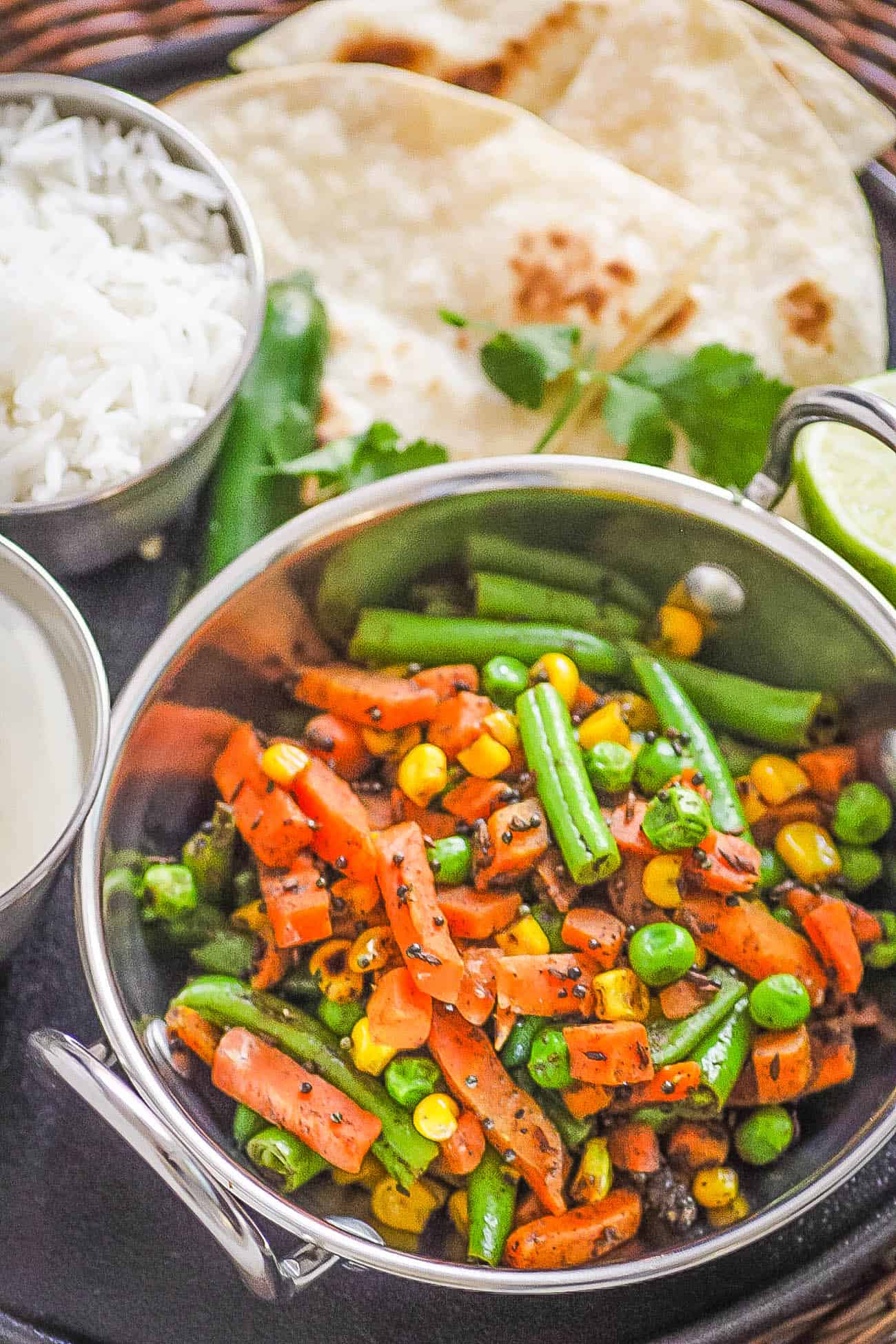 indian vegetables served in a stainless steel pot with naan and rice on the side