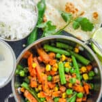 indian vegetables served in a stainless steel pot with naan and rice on the side