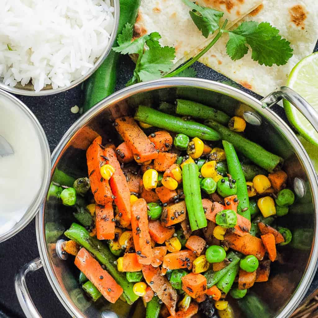 indian vegetables served in a stainless steel pot with naan and rice on the side