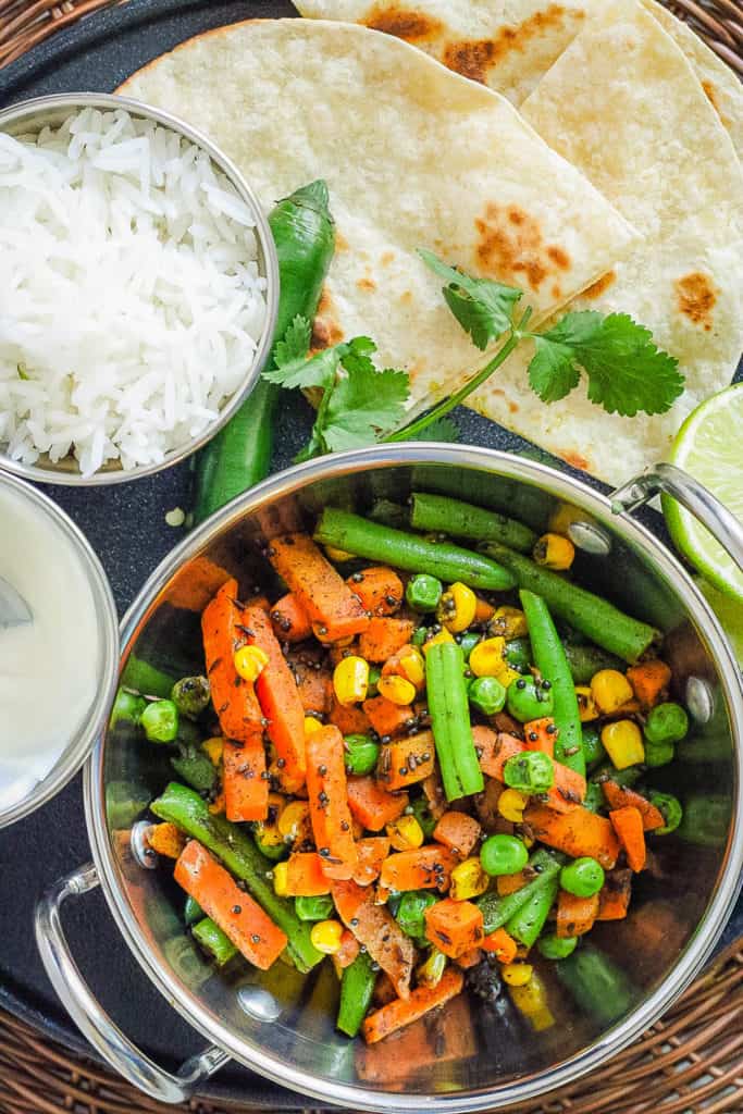 indian vegetables served in a stainless steel pot with naan and rice on the side