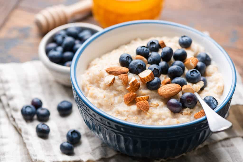 Oatmeal with blueberries and almonds in blue ceramic bowl on a wooden table. 