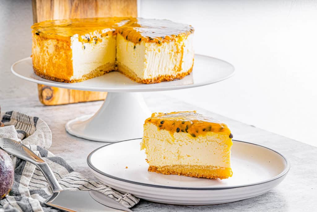 slice of passionfruit cheesecake on a plate with whole cheesecake in the background