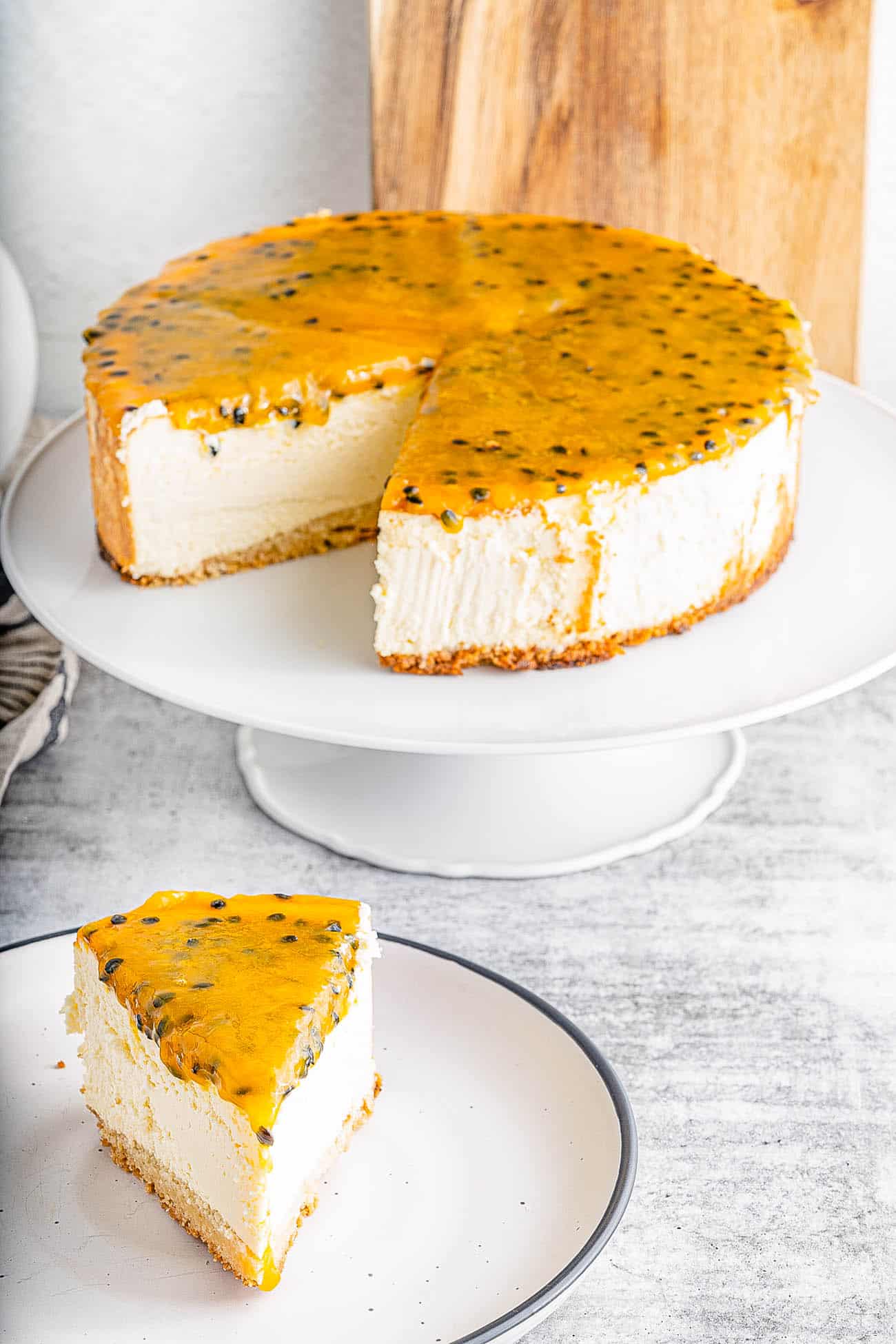 slice of passionfruit cheesecake on a plate with whole cheesecake in the background