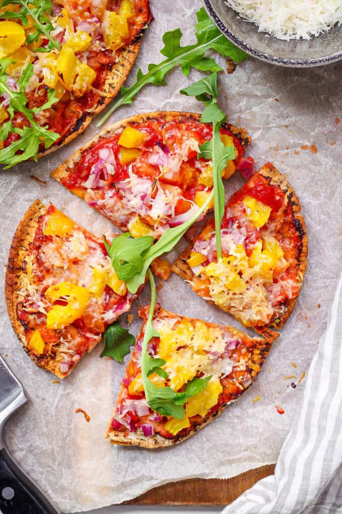 healthy homemade pita pizza / pita bread pizza with veggies as toppings on a cutting board
