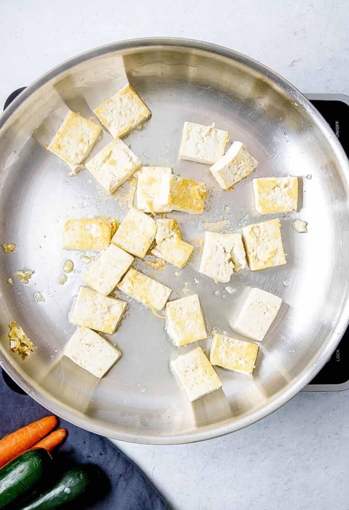 Tofu sauteeing in a pan.