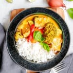 vegan panang curry in a black bowl with fresh herbs and rice