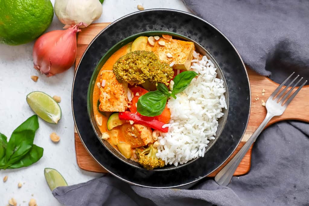 vegan panang curry in a black bowl with fresh herbs and rice