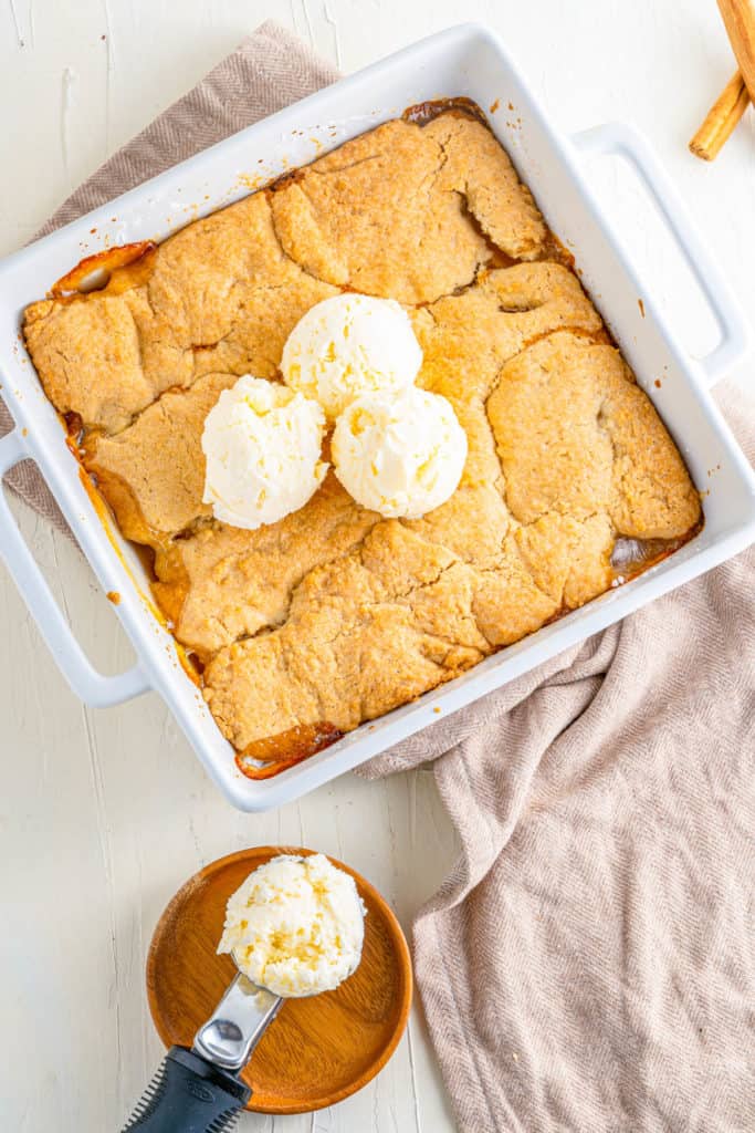 Vegan Peach Cobbler in a baking dish topped with ice cream