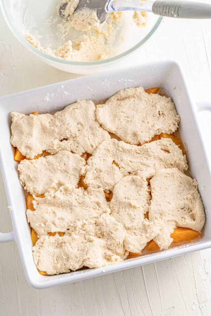 cobbler topping added to peaches in a baking dish