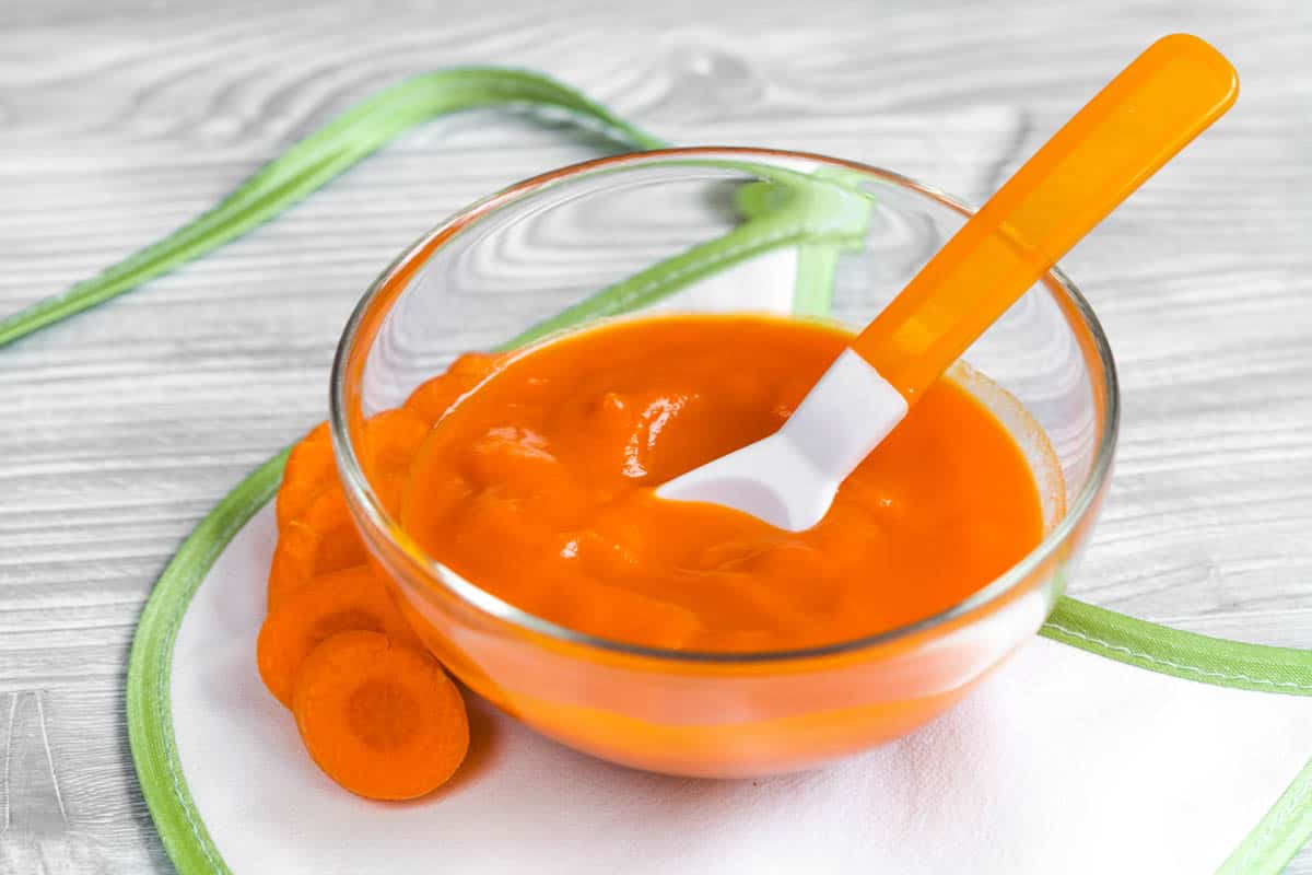 Carrot baby food puree served in a gl، bowl with a s،.