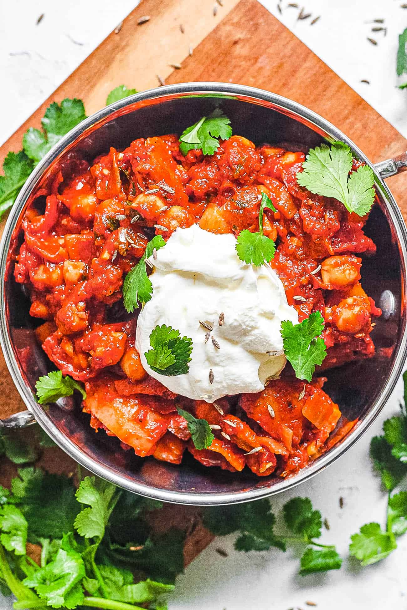 chana masala served in a silver bowl with yogurt and cilantro