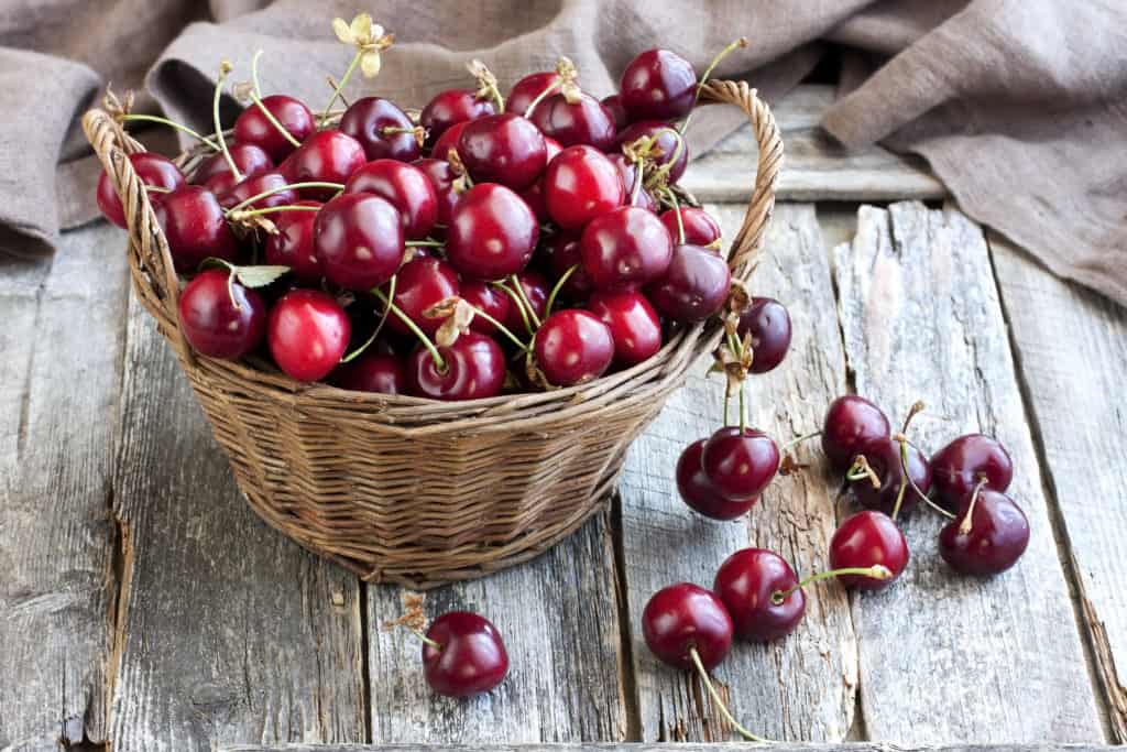 Wicker basket with cherries on wooden background - foods that start with c