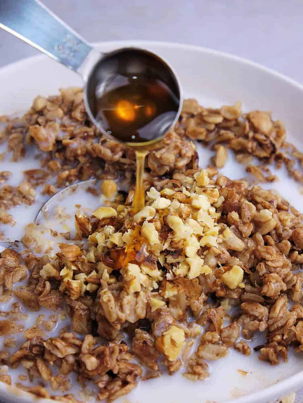 Maple syrup added to oatmeal bowl with milk, walnuts, and cocoa powder.