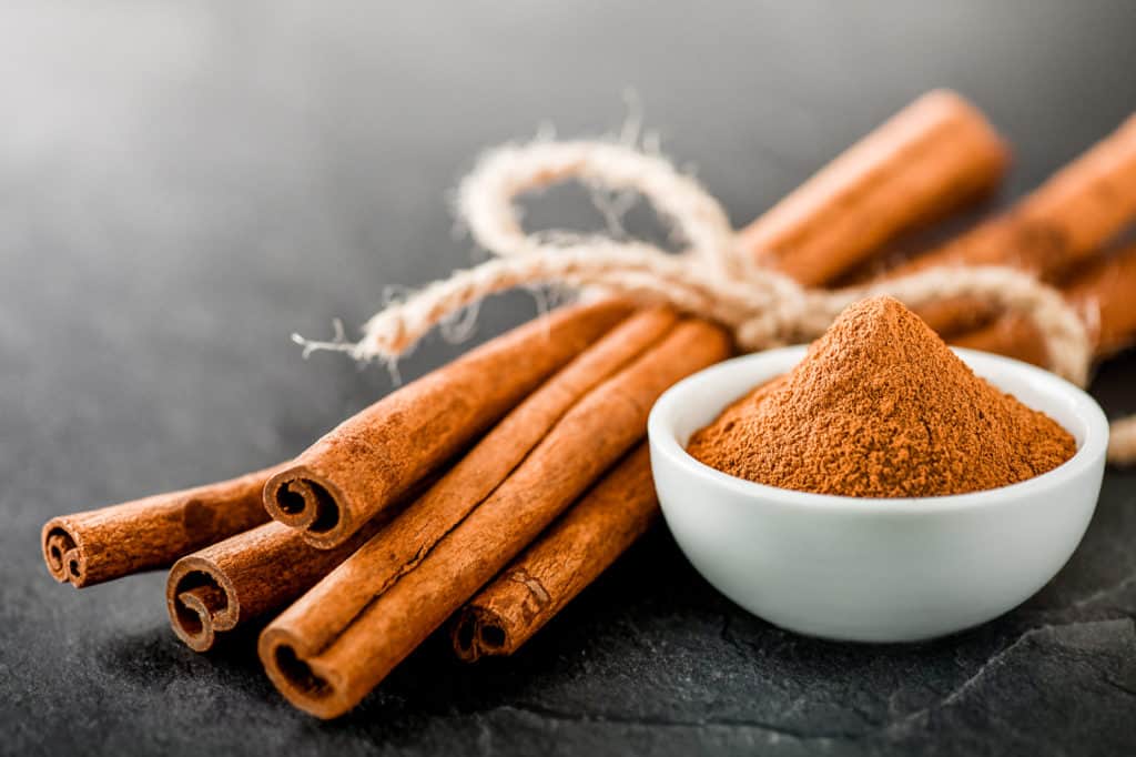 foods that start with c - Cinnamons dried sticks on dark stone table. Cinnamon ginger powder in white bowl on black board.