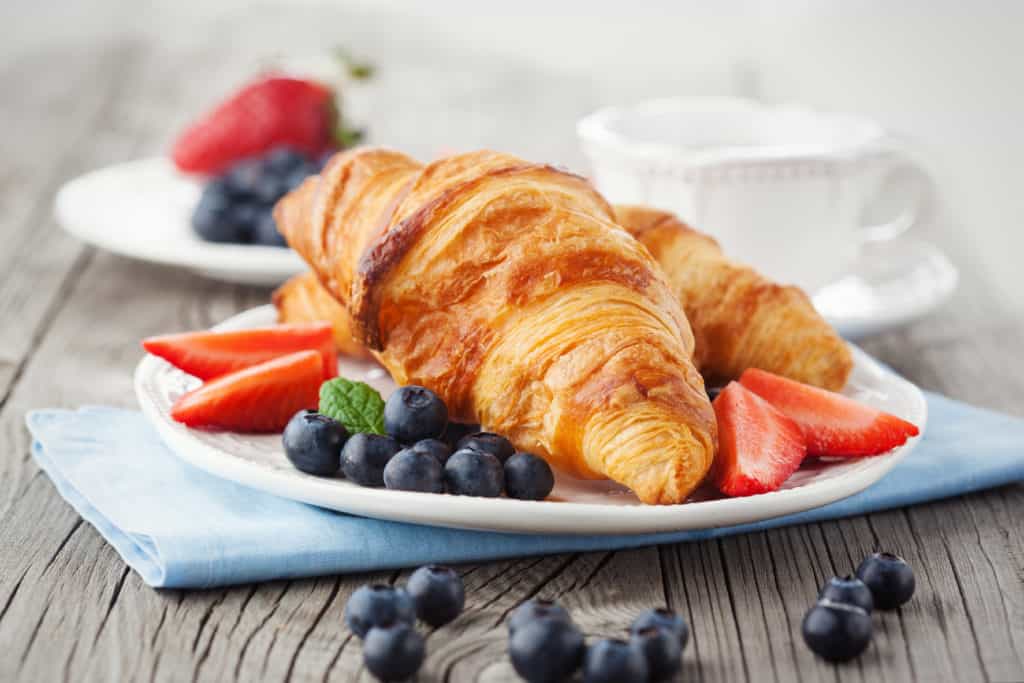 Delicious breakfast with fresh croissants and ripe berries on old wooden background