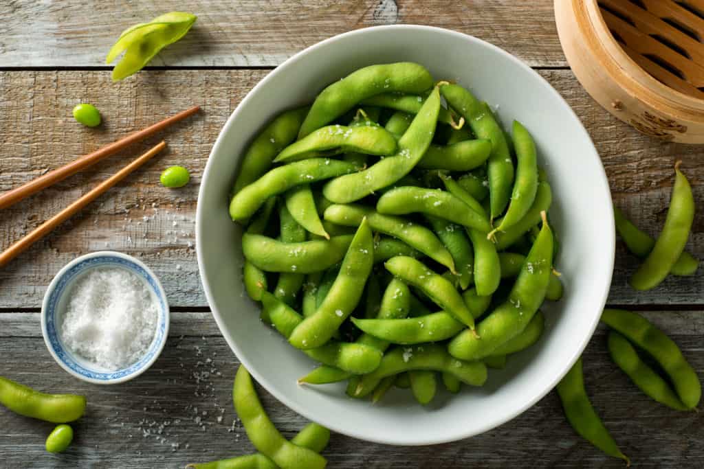 foods that start with E - Fresh steamed edamame sprinkled with sea salt on a rustic tabletop.