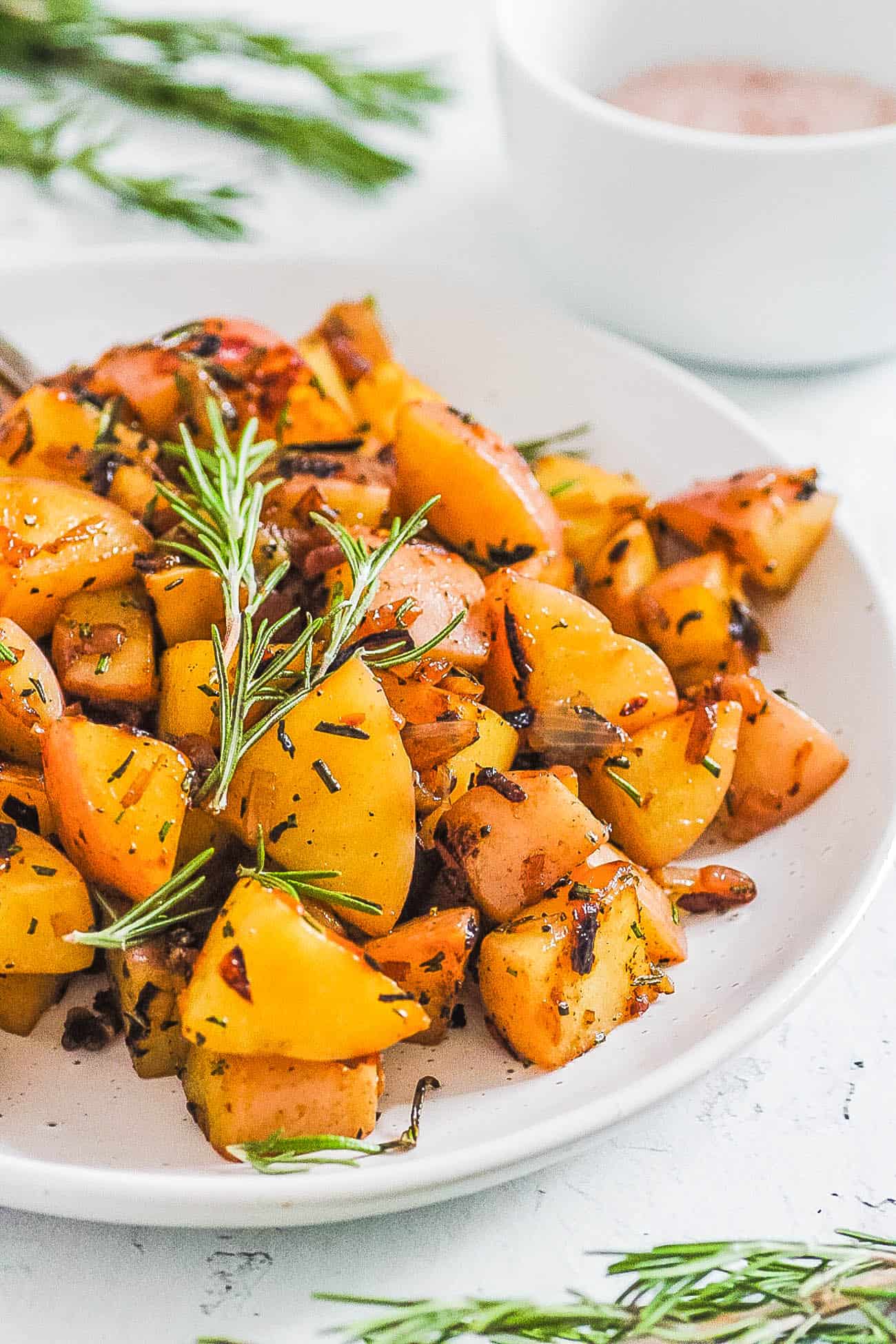 fried potatoes and onions served on a white plate with rosemary on top