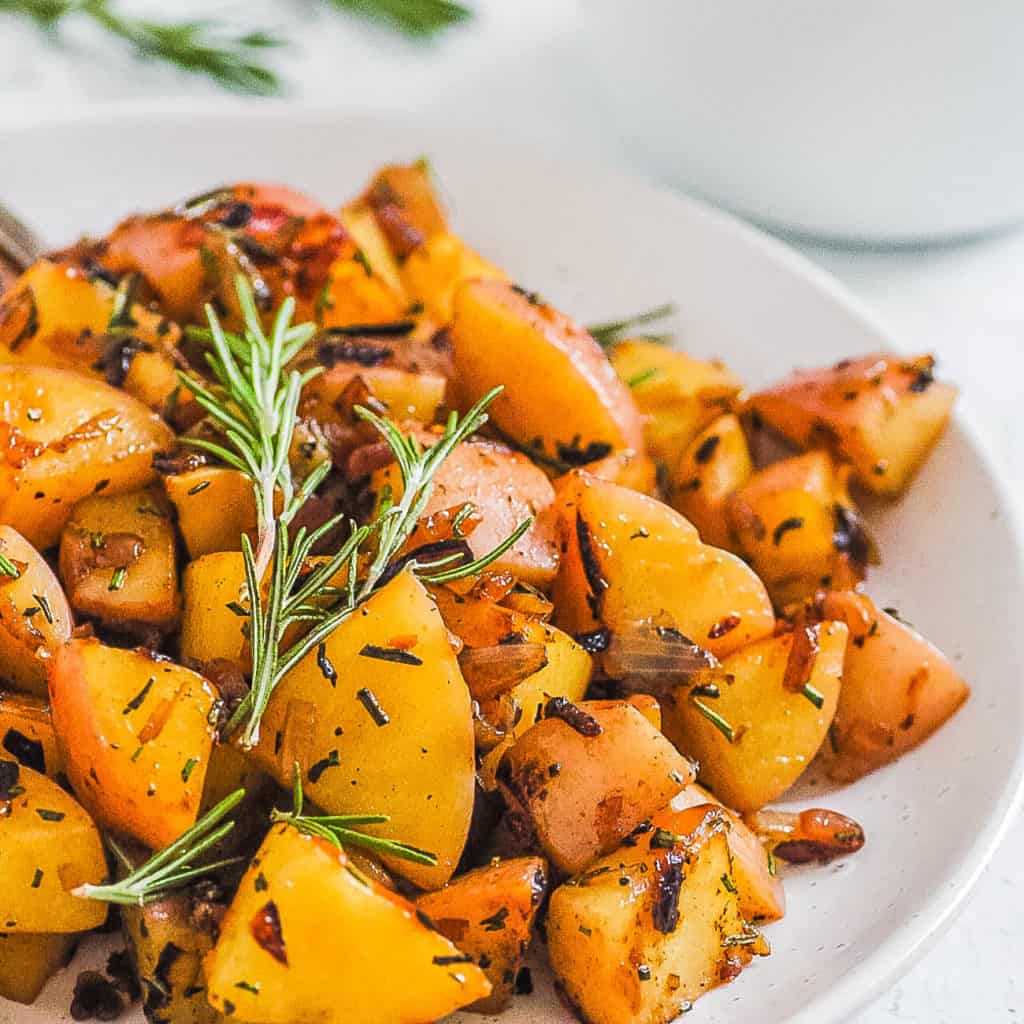 fried potatoes and onions served on a white plate with rosemary on top