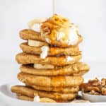 Healthy Pancakes stacked on a white plate with oatmeal and bananas and nuts and syrup