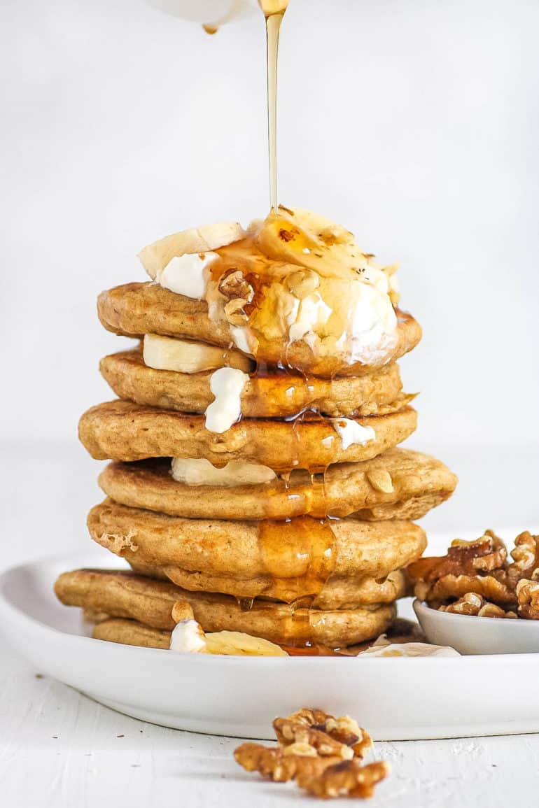 Healthy Pancakes stacked on a white plate with oatmeal and bananas and nuts and syrup