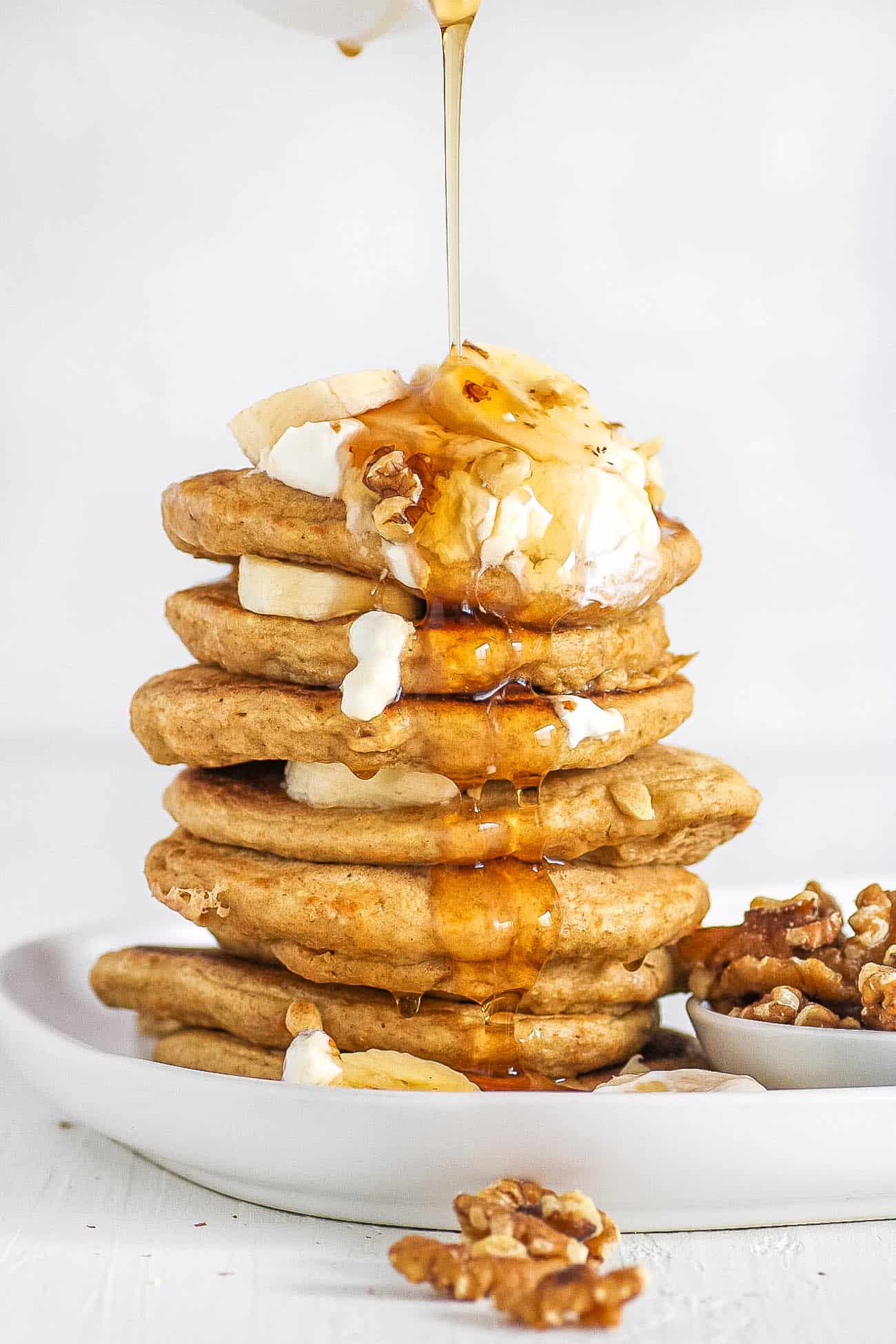 Healthy Pancakes stacked on a white plate with oatmeal and bananas and nuts and syrup