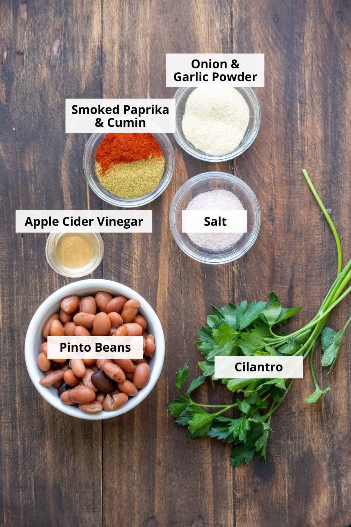 Bowls of beans, spices and fresh cilantro on a wooden surface