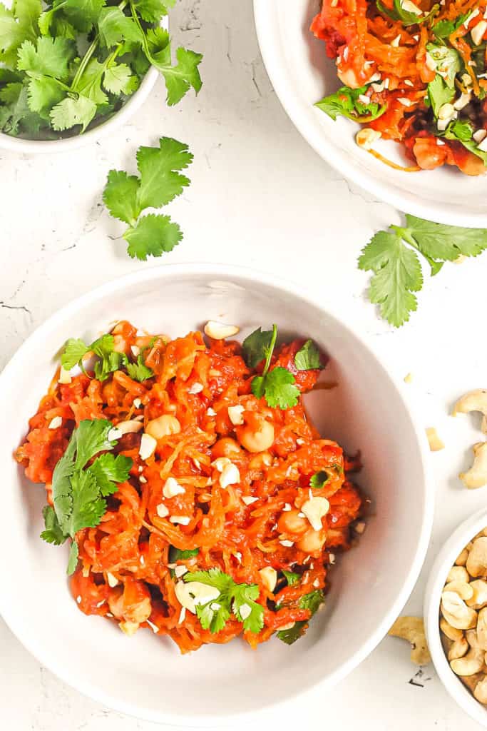 curry spaghetti squash tossed with spices herbs and cashews in a white bowl