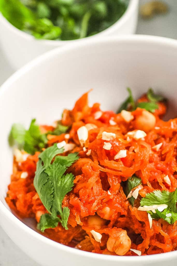 curry spaghetti squash tossed with spices herbs and cashews in a white bowl