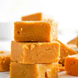 Microwave peanut butter fudge cut into squares, stacked on parchment paper.