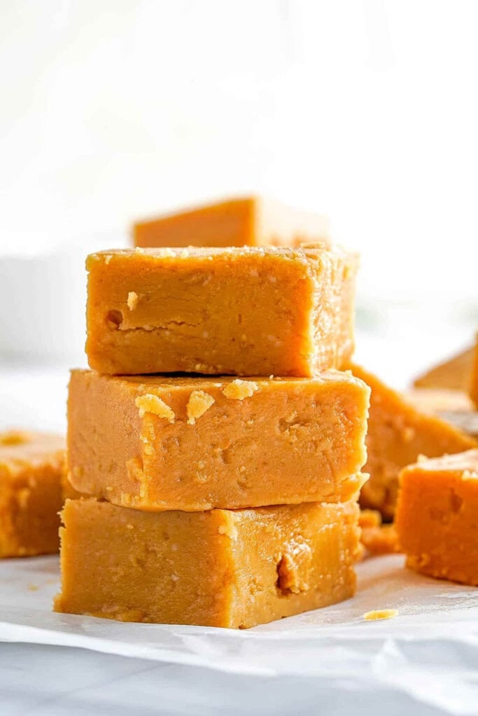 Microwave peanut butter fudge cut into squares, stacked on parchment paper.