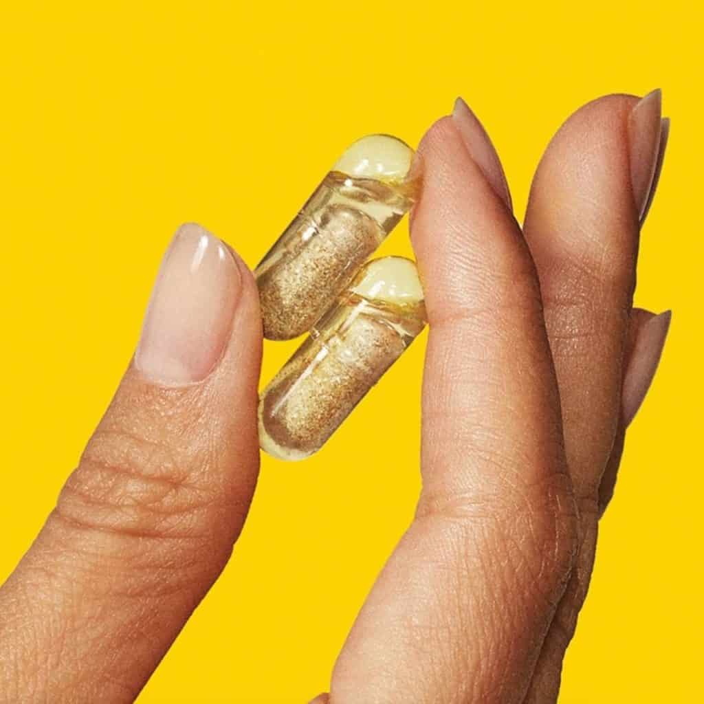 Two fingers holding two vitamin capsules on yellow background