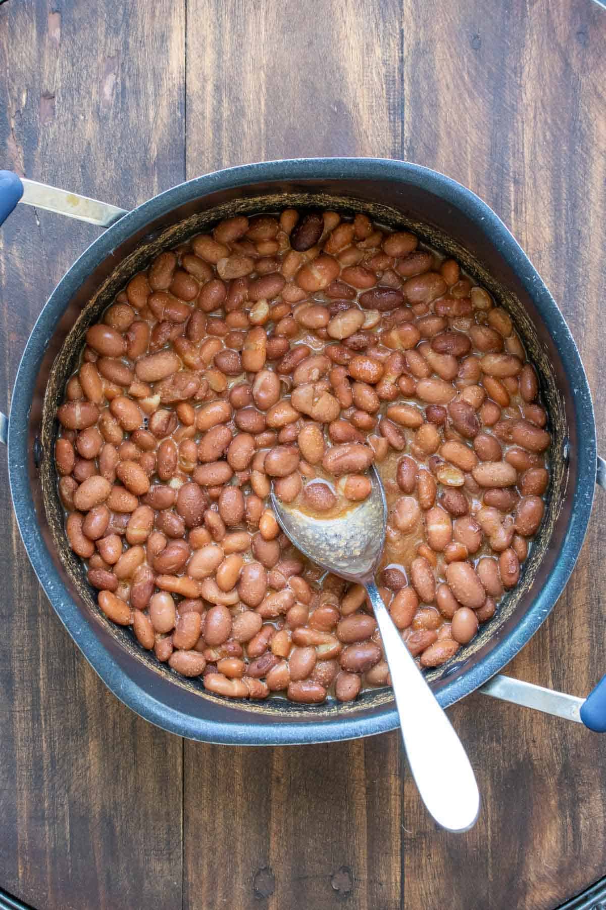 whole pinto beans with seasonings in a large pot with silver spoon.