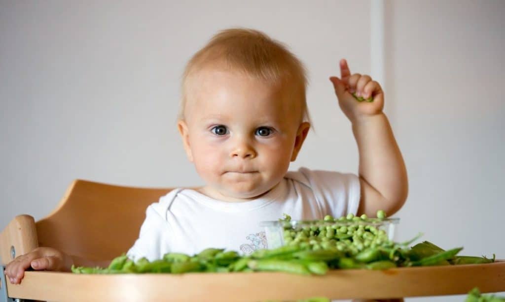 Baby in high chair with green beans and peas.