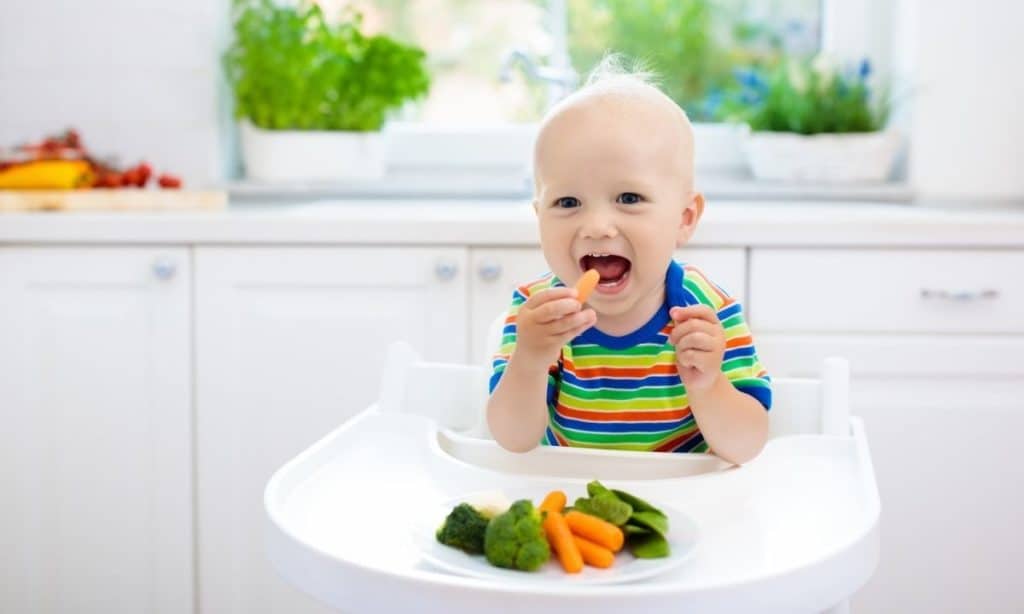 Baby in high chair with carrots, broccoli, and snap peas.