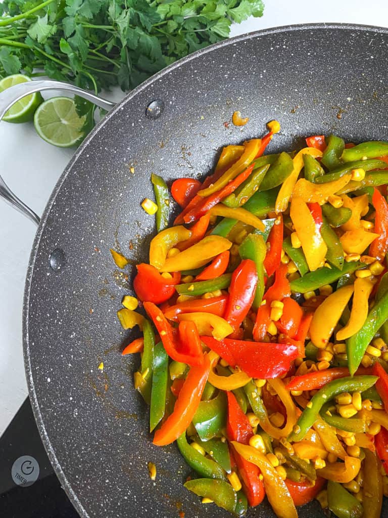 peppers and corn cooking with taco seasoning in a pan