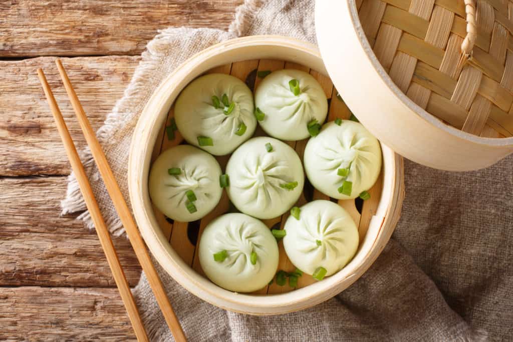 Traditional chinese baozi steam buns in a bamboo steamer basket close-up on the table. Horizontal top view from above